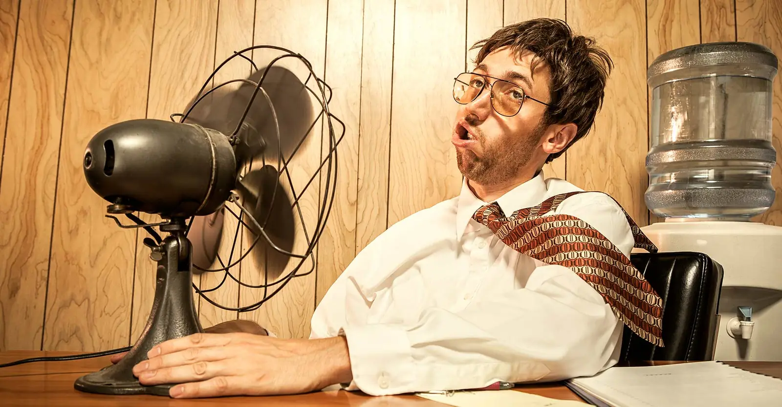 Employé de bureau assis devant un ventilateur, en pleine chaleur