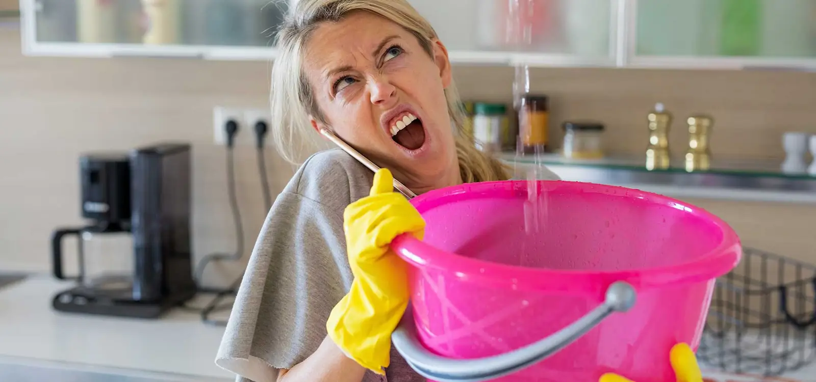 Femme au téléphone recueillant une fuite d’eau dans une bassine